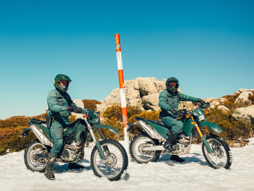 Two Guardia Civil Seprona agents on motorcycles patrol mountainous terrain under clear sky.