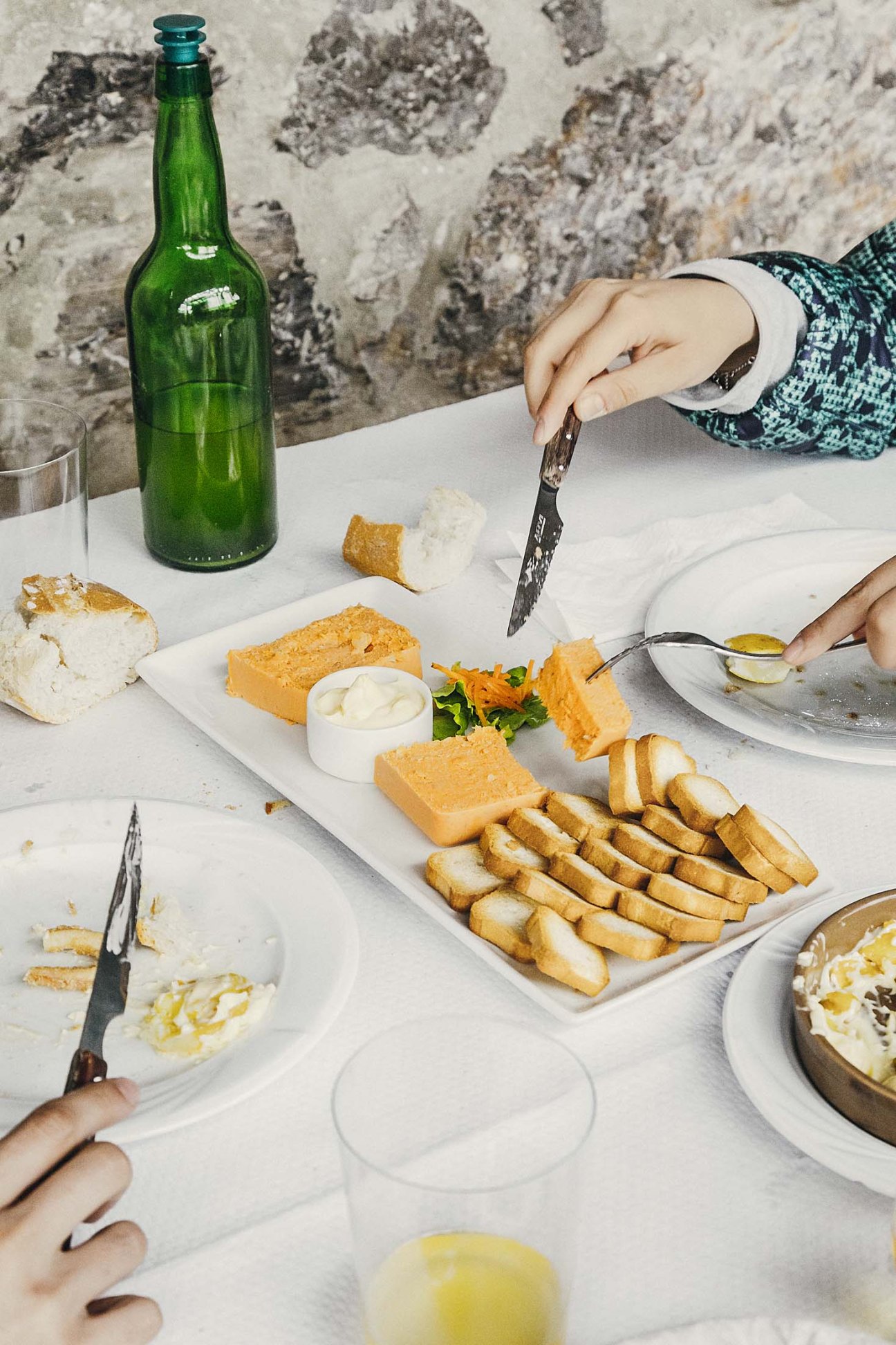 Large portions of food served at a white table including bread, fried potatoes, and seafood with a green beer bottle