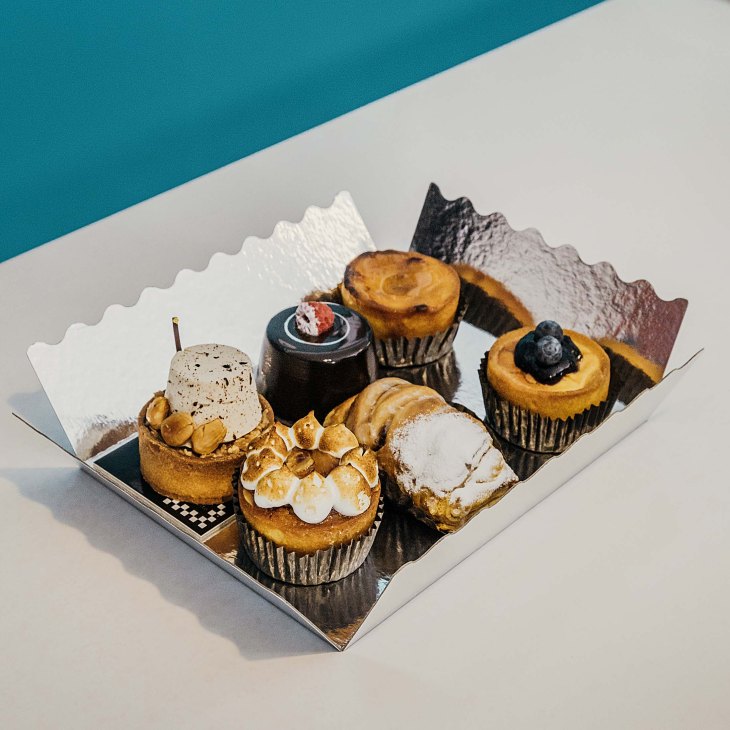 Assortment of low-sugar cakes and pastries displayed in a white box with decorative mountain backdrop