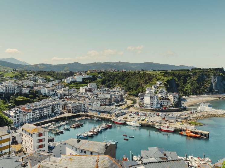 Aerial view of the coastal town of Luarca with its harbor, colorful buildings, and surrounding mountains in Asturias, Spain.