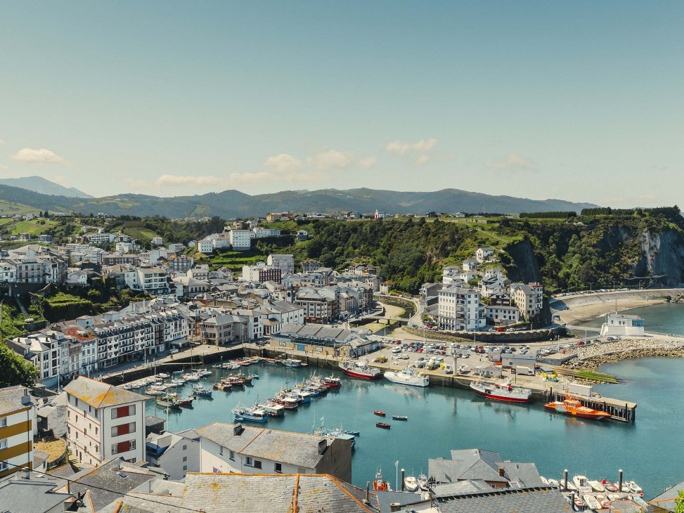 Aerial view of the coastal town of Luarca with its harbor, colorful buildings, and surrounding mountains in Asturias, Spain.