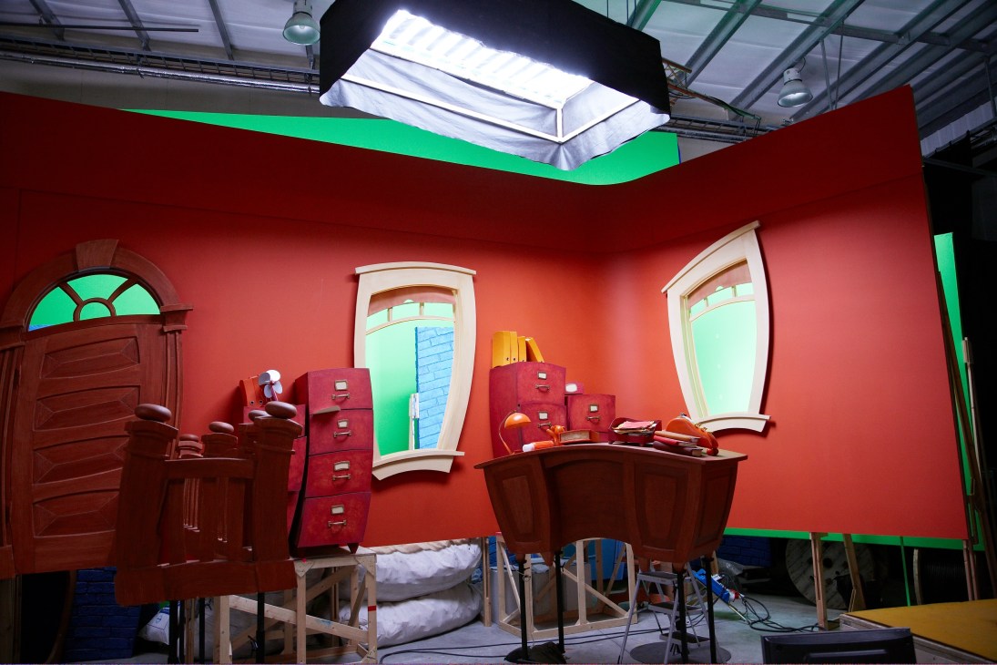 Colorful LazyTown set with red walls, green trim, stylized furniture and window props under bright studio lighting.