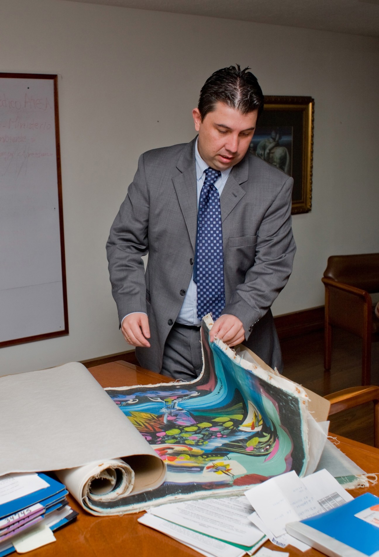 DNE investigator examines confiscated paintings by Colombian artist Alejandro Obregón at a desk.