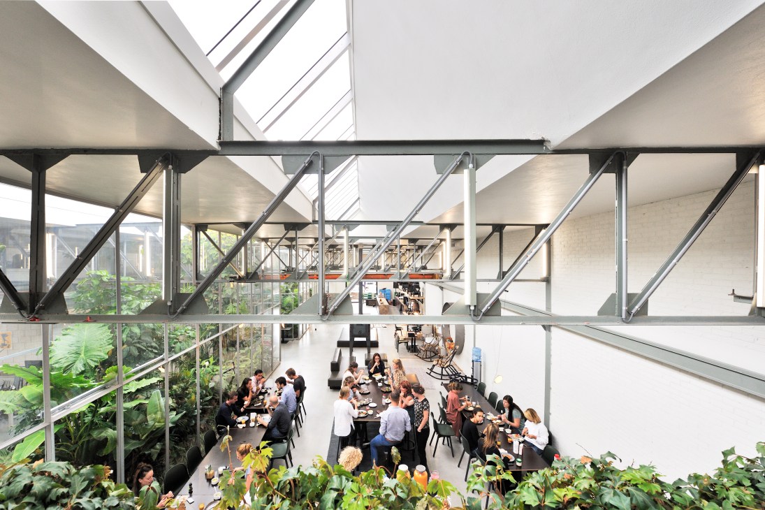 Staff members gathered around a long black dining table for lunch in an open office space with industrial architecture