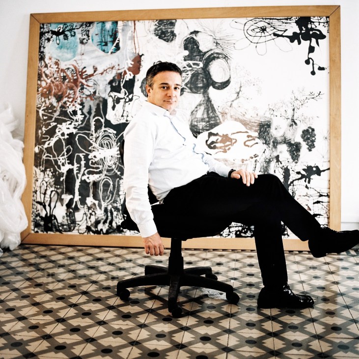 Quim Vila sits on a black chair in front of an abstract black and white artwork with a wooden frame.