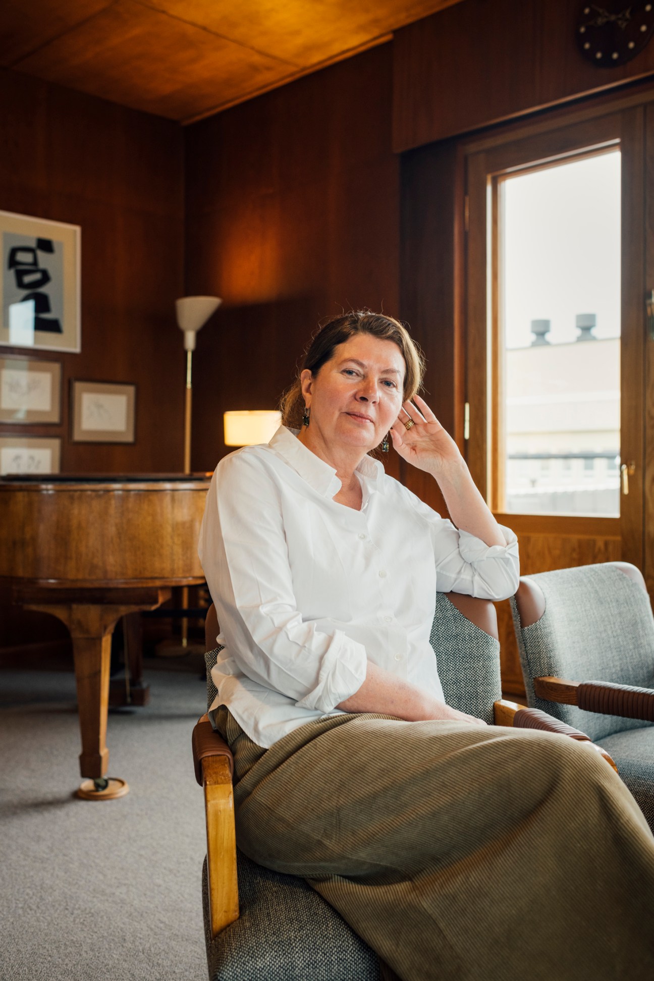 Ilse Crawford sitting in an upholstered chair in a warm wood-paneled room with framed artwork