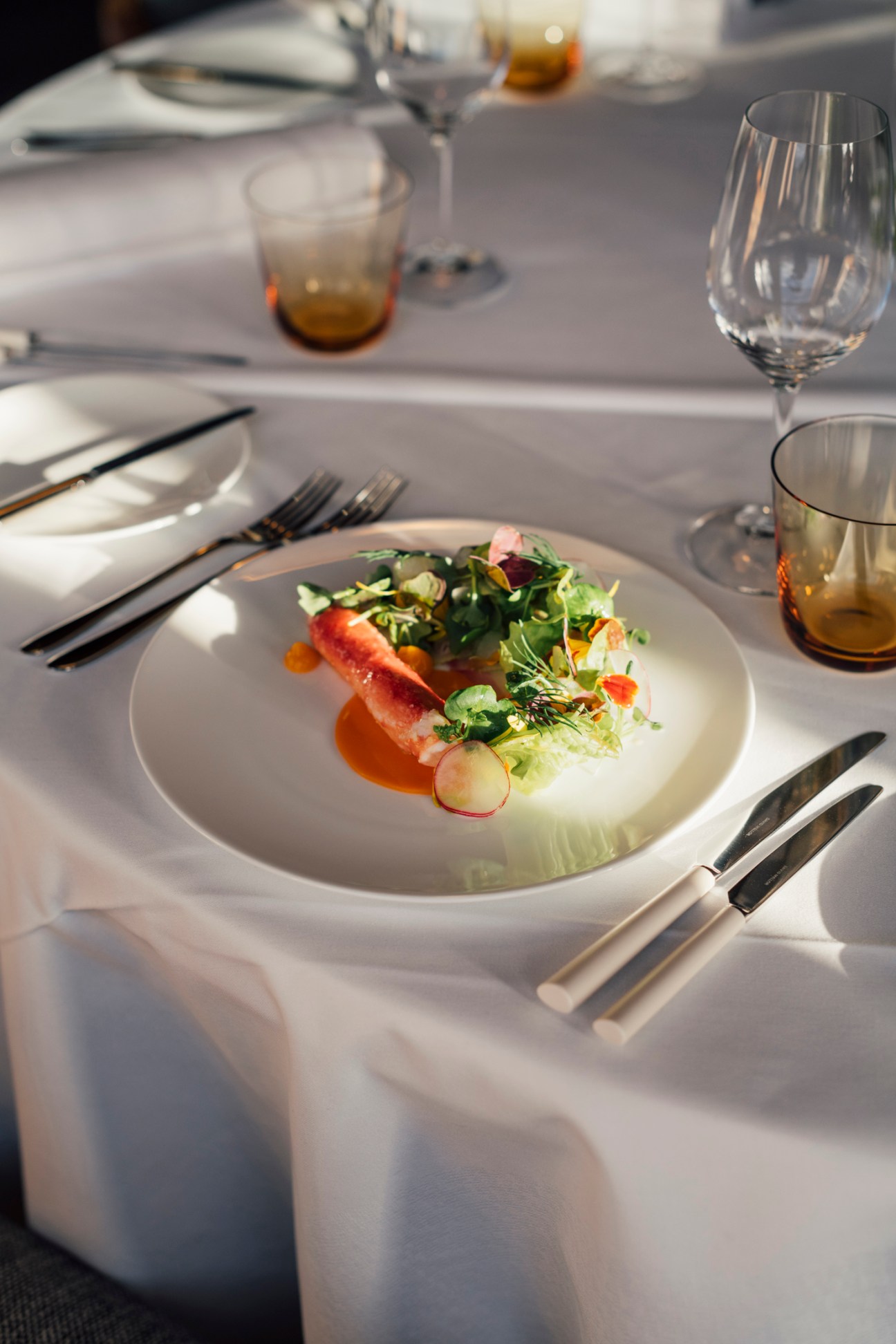 Crudité salad and king crab dish plated on white dinnerware with wine glass and elegant table setting