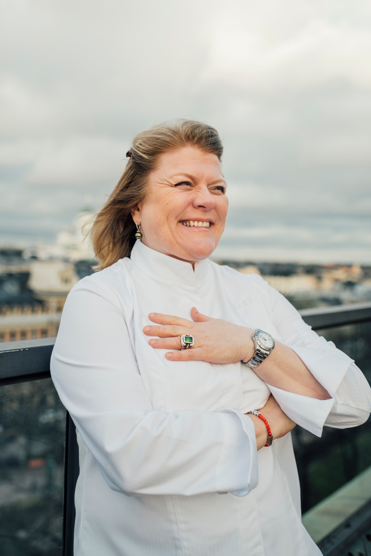 Helena Puolakka standing outdoors in chef's whites, smiling and looking to the side with arms crossed