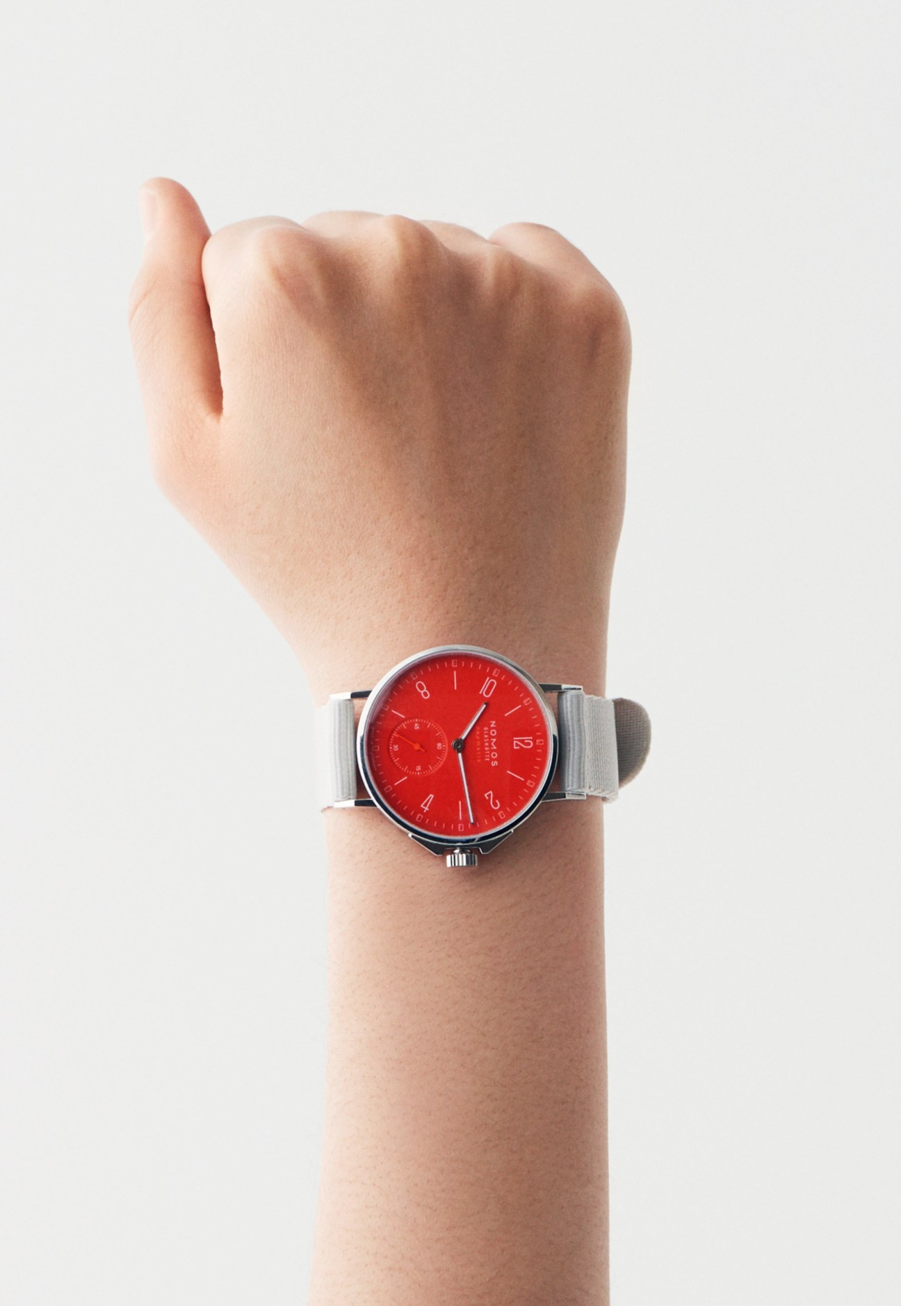 Wrist wearing a Nomos Glashütte watch with red dial and grey fabric band.