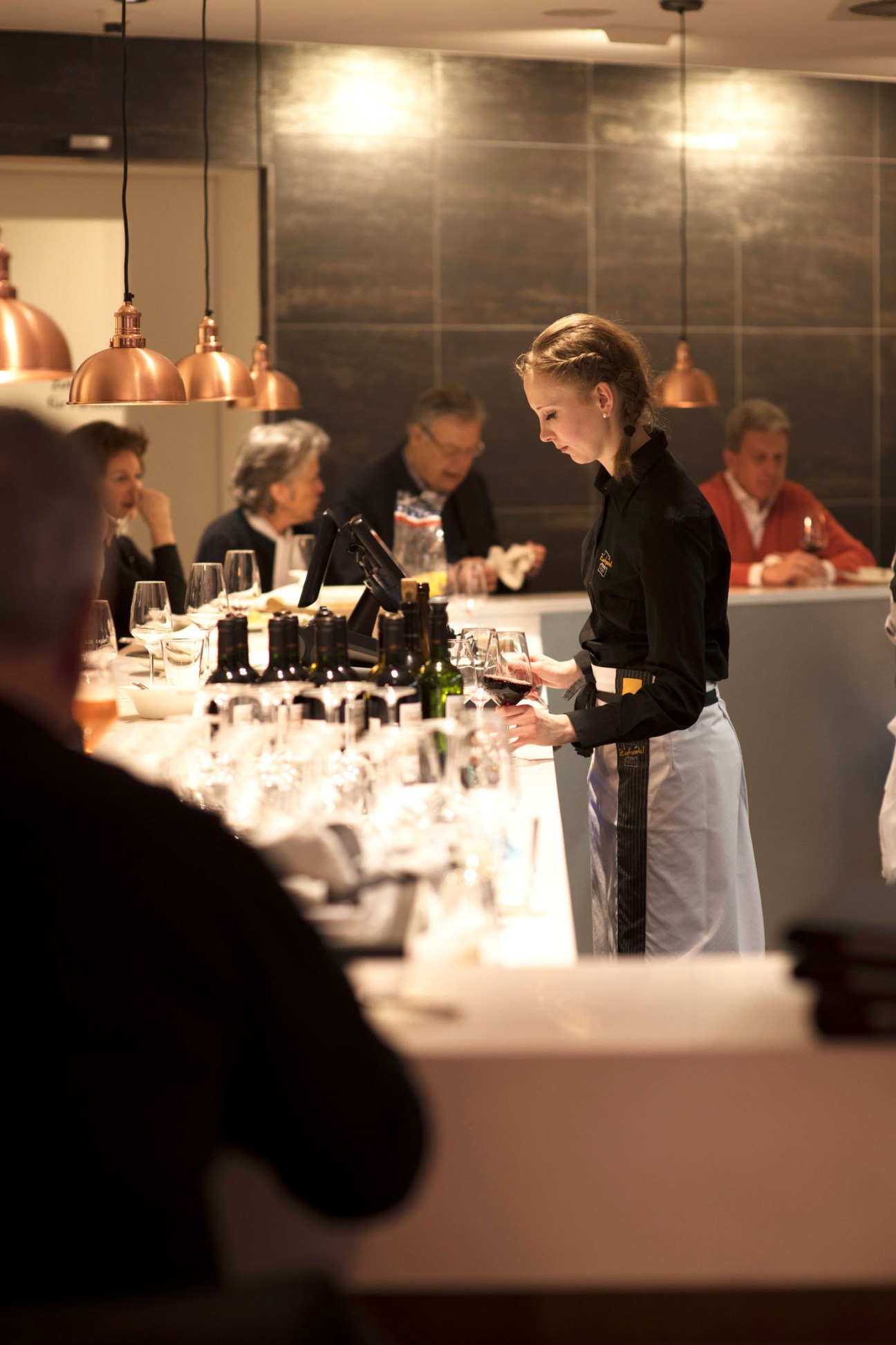 A server in black uniform and white apron serves guests at Zurheide's premium-beef bar under copper pendant lights.