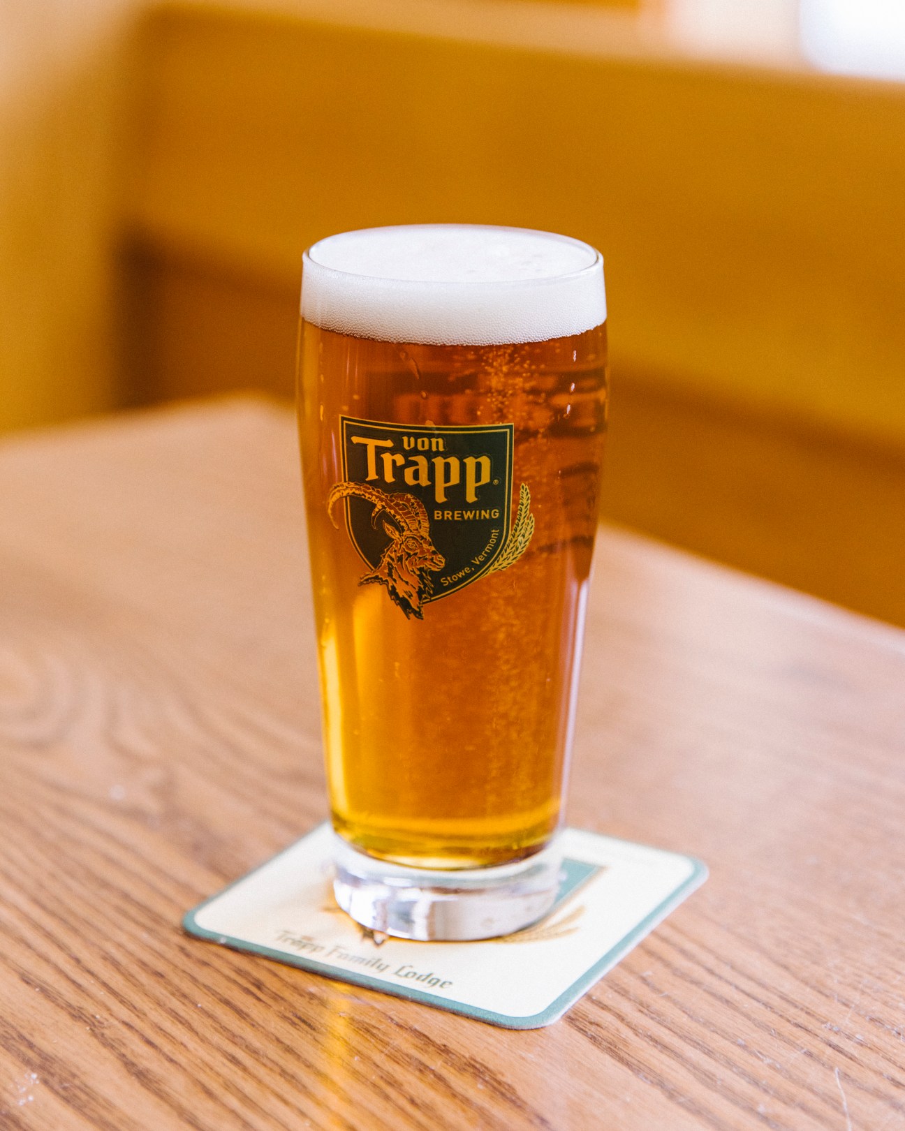 A glass of Von Trapp brewing beer with foam head sitting on a wooden table with coaster