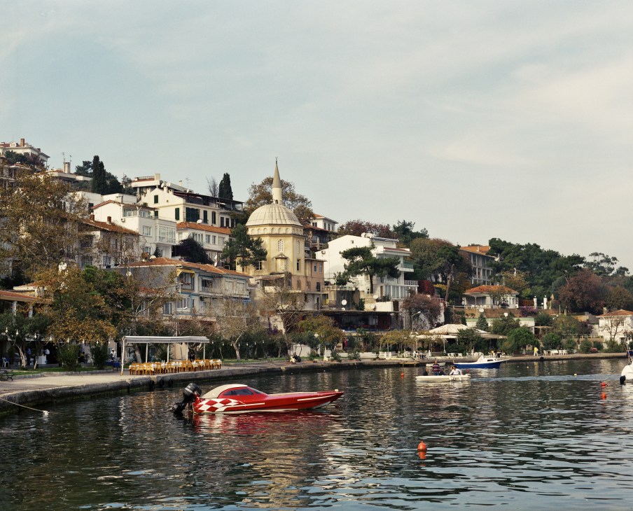 Waterfront view of Burgazada island with historic buildings, a yellow-domed mosque, and a red speedboat moored in the water.