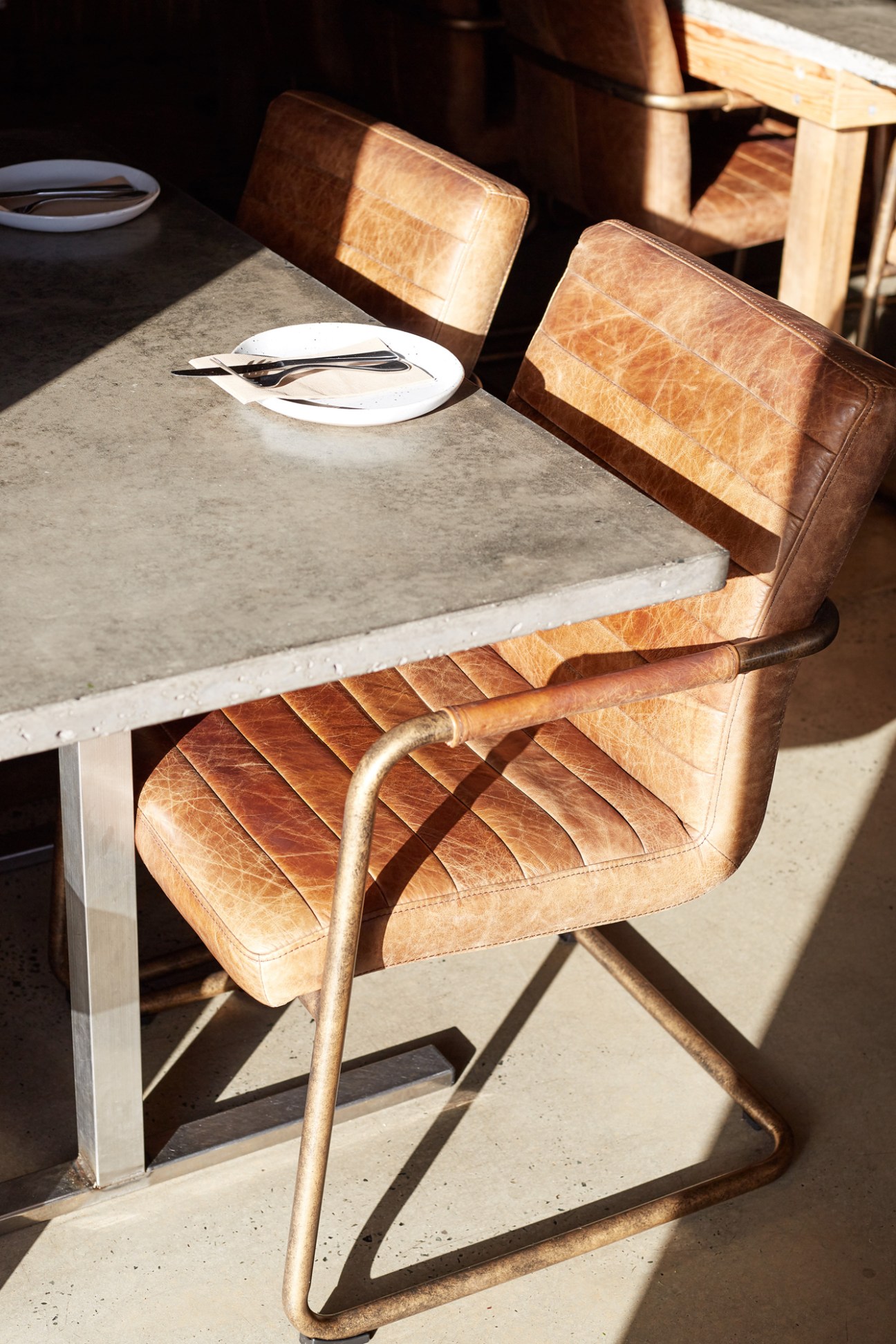 Tan leather chairs at a concrete table set with white plate and cutlery at Paradiso bar in Yamba.