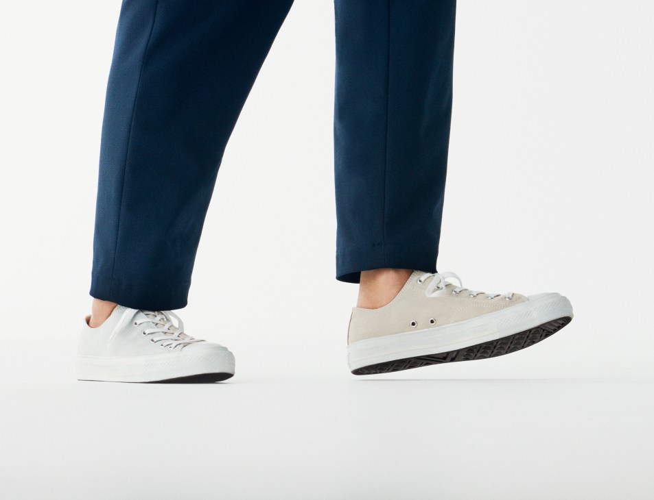 Person wearing navy trousers and white canvas trainers by MoonStar x Édifice shown from waist down.