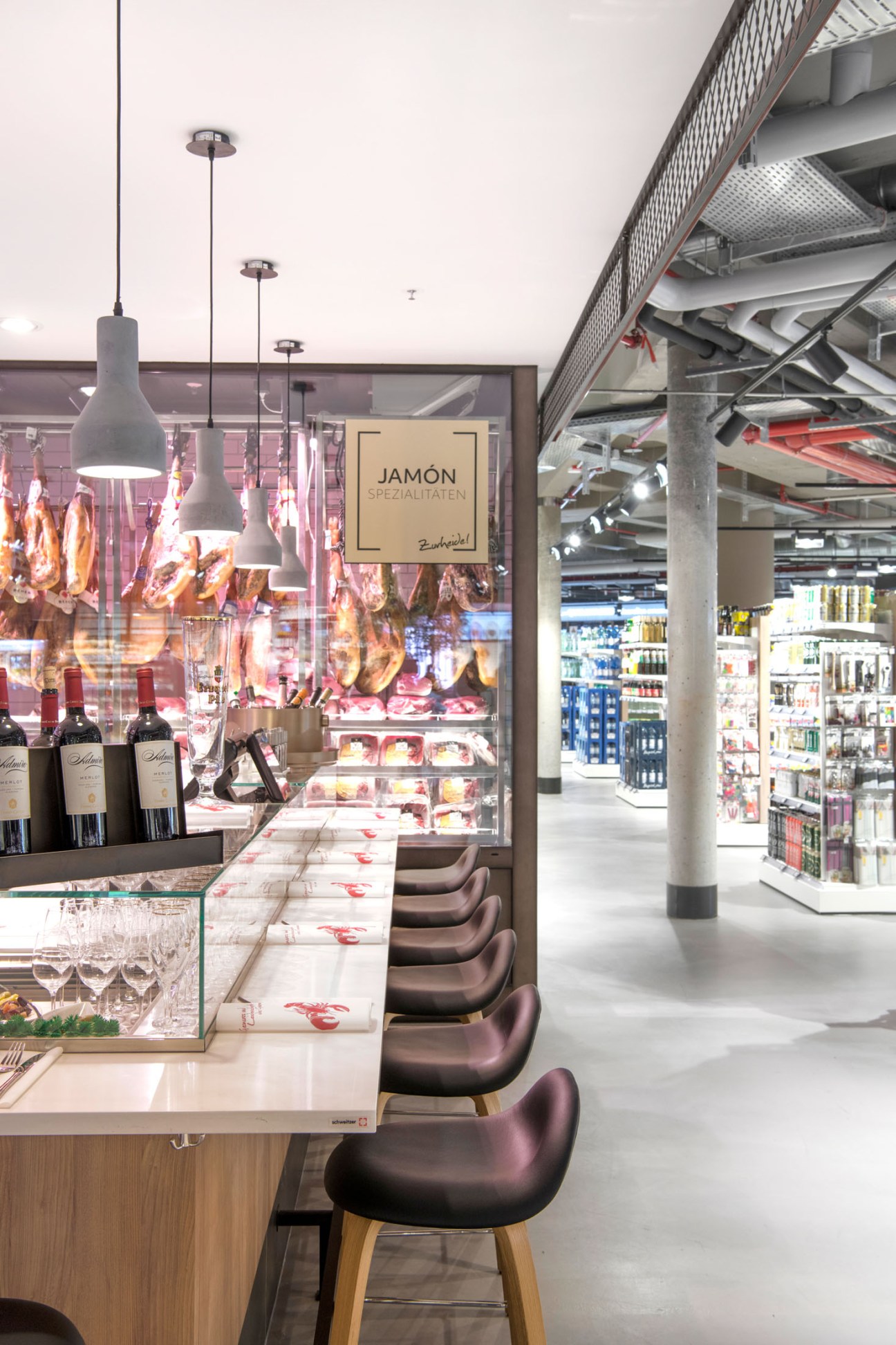 Zurheide's jamón bar with hanging Spanish ham, bar seating, wine bottles, and pendant lighting.