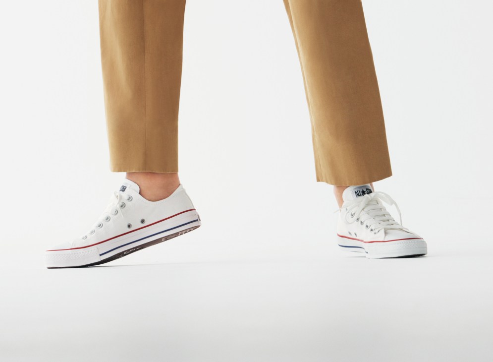 Person wearing tan cropped trousers and white Converse trainers with red and navy stripe detail.