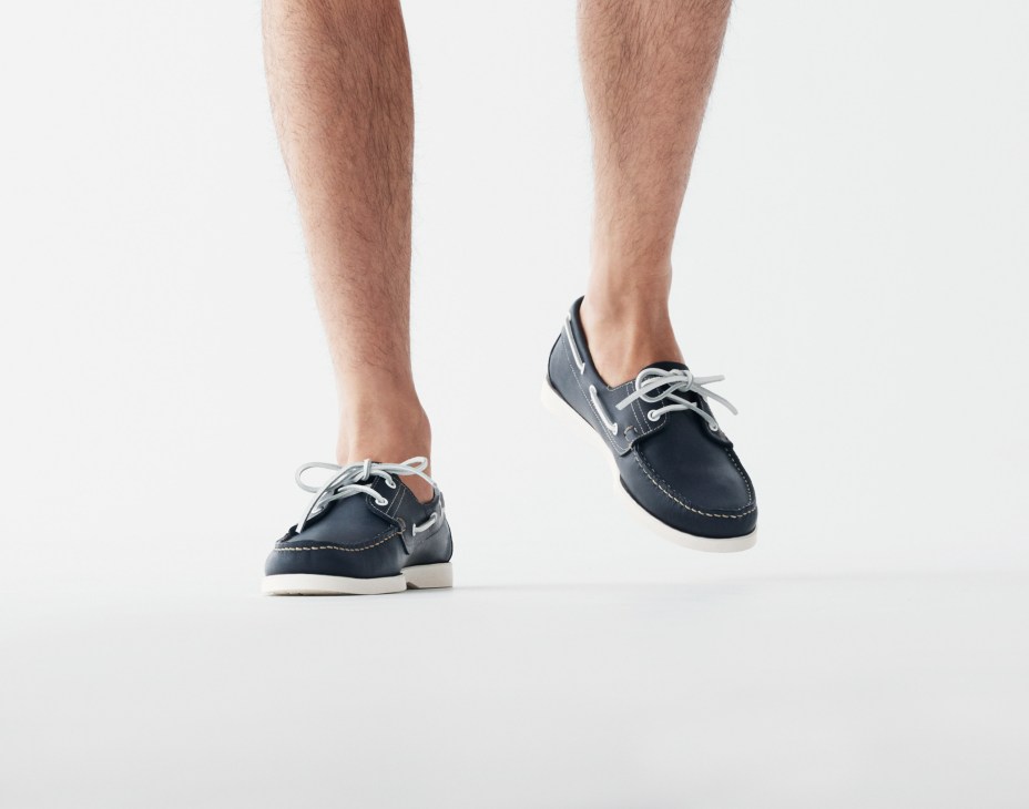 Close-up of a man's feet wearing navy blue Paraboot boat shoes with white laces and soles.