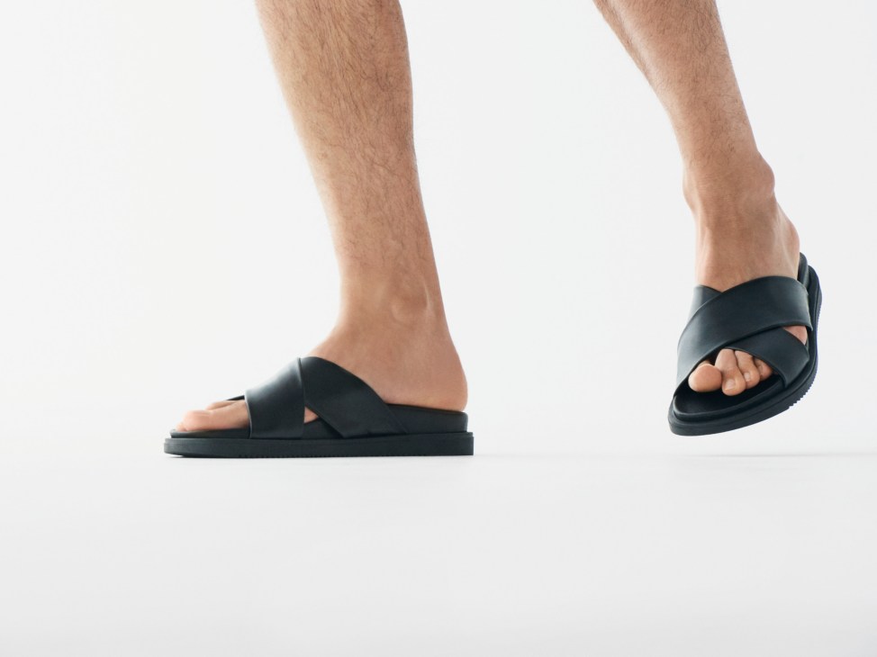 Black leather sandals with crossover straps and cushioned sole on male feet.
