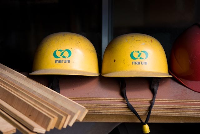 Two yellow hard hats with Maruni company logo displayed on a shelf in the factory.