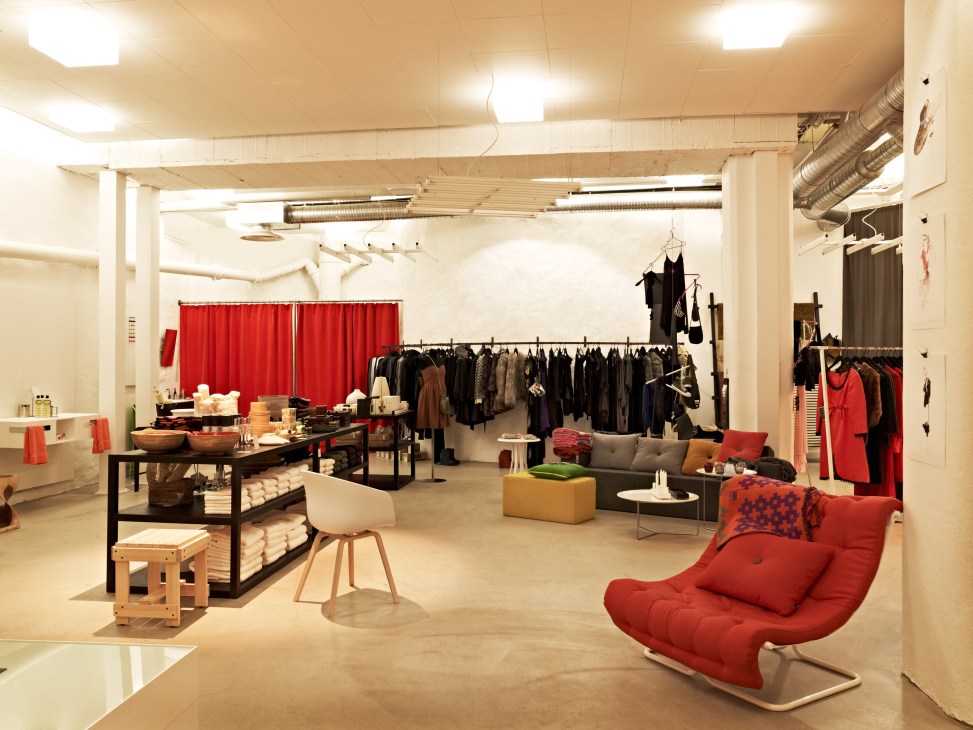 Interior of van Deurs et al fashion store with clothing racks, red curtains, furniture displays, and seating area.