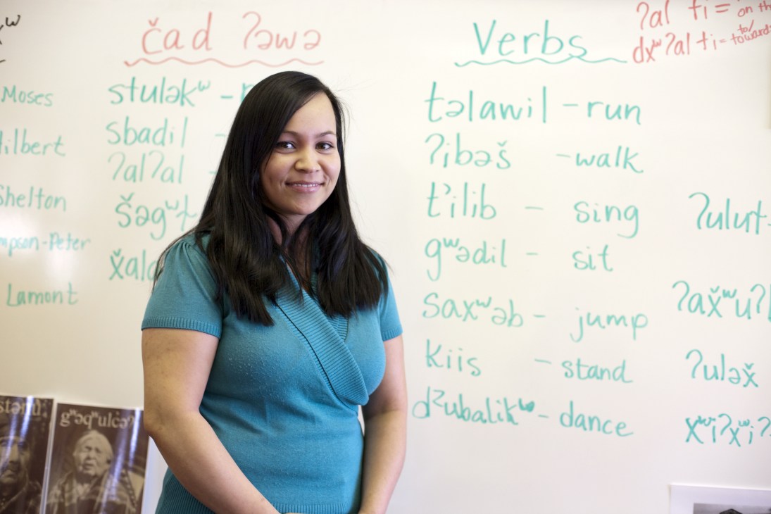 Teacher Natosha Gobin stands in front of a whiteboard displaying Lushootseed language lessons with verbs and words written in green and red chalk.