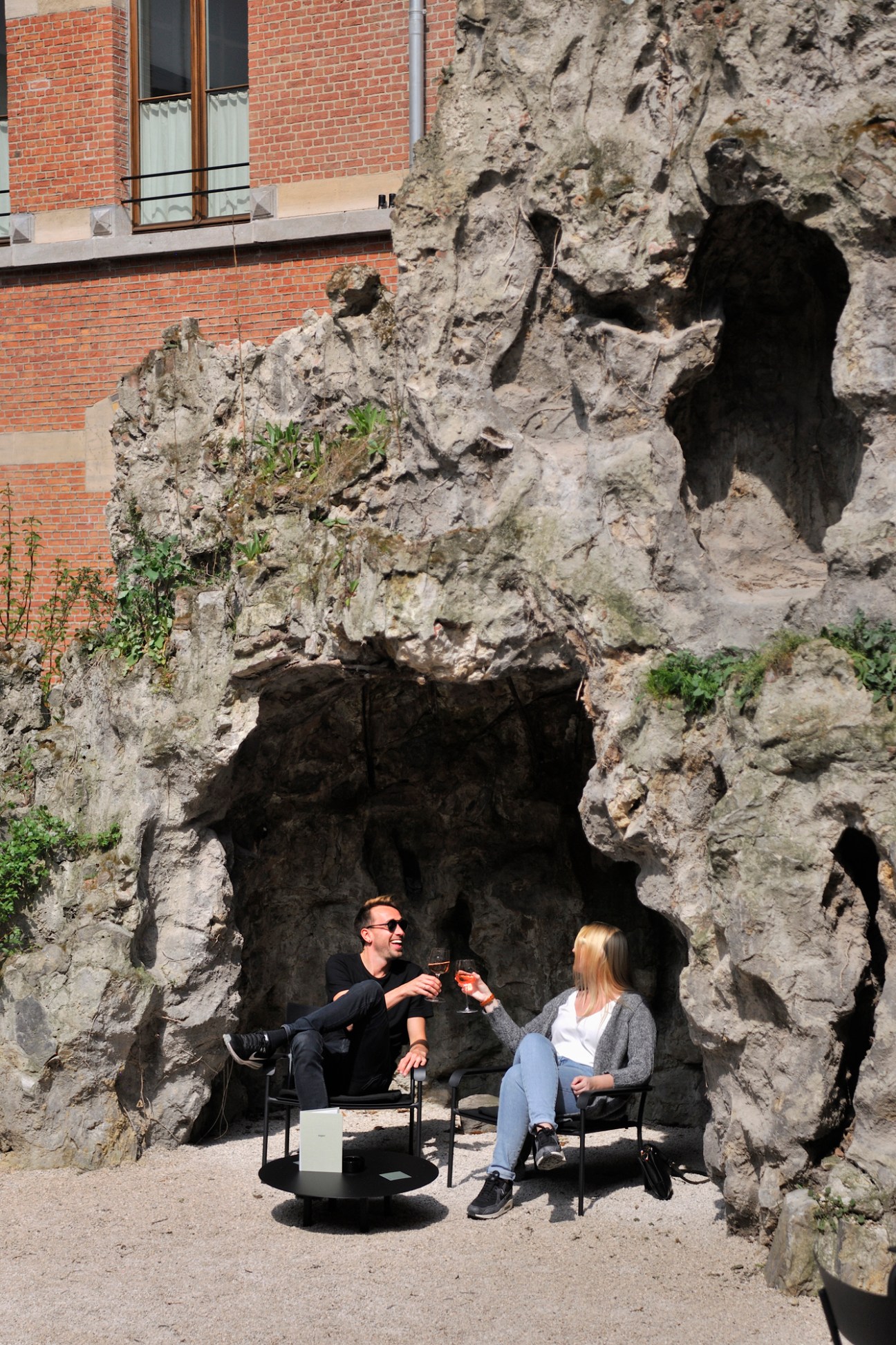 Two people sit in chairs inside a historic grotto with weathered stone walls and natural cave openings.