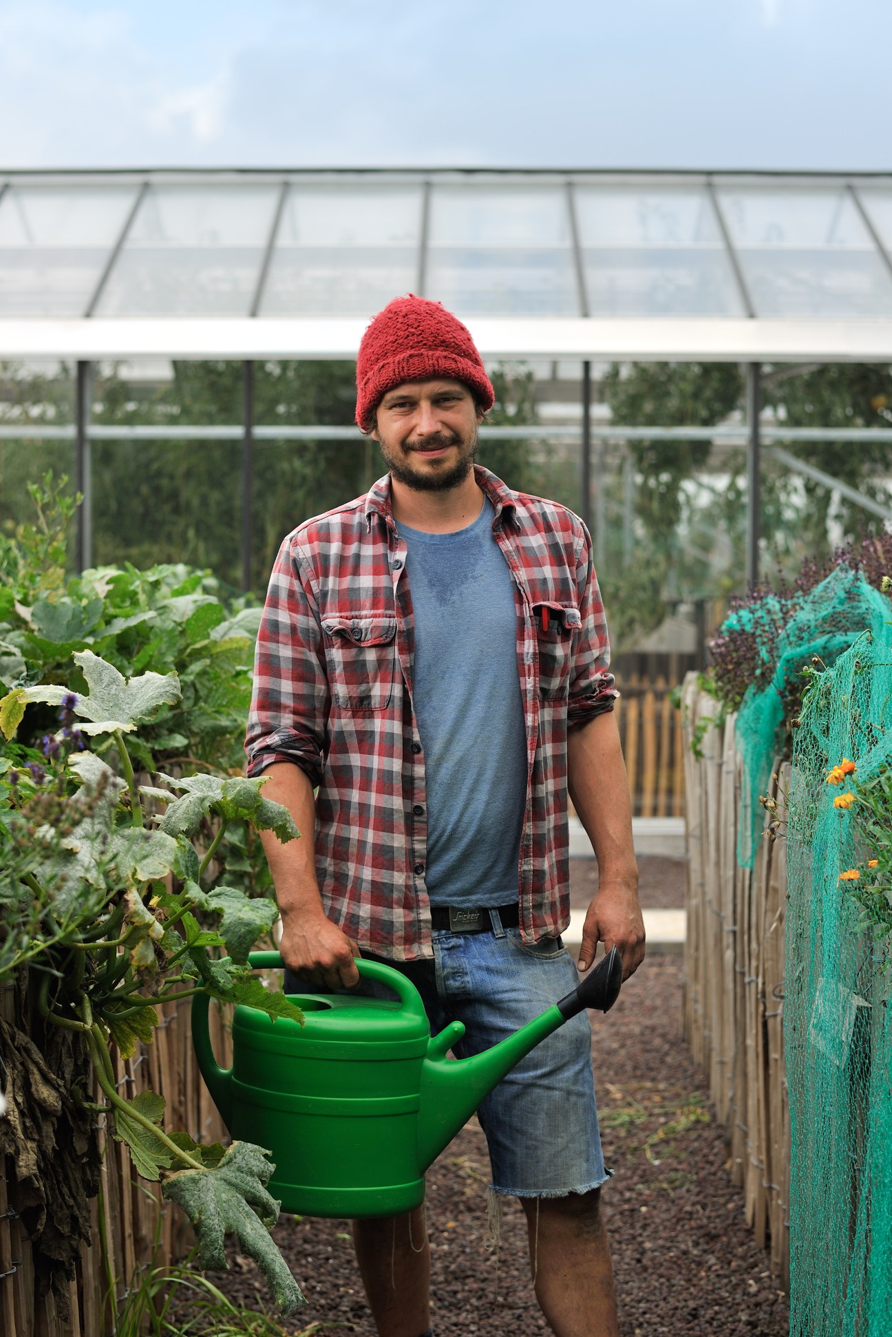 Farmer Bram Stessels holding a green watering can in a greenhouse at Pakt's rooftop garden
