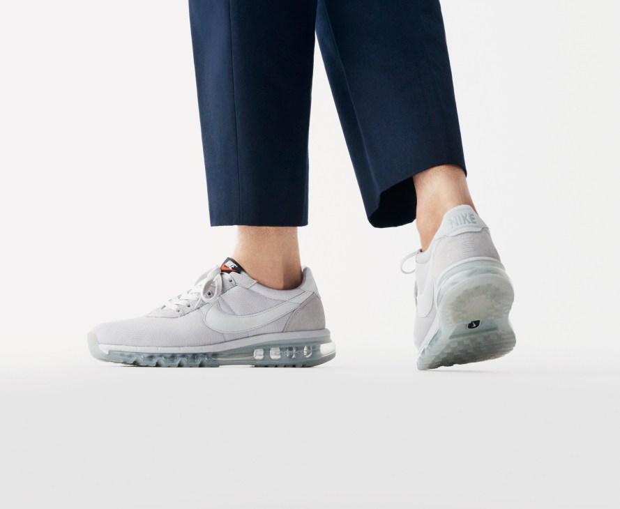 Person wearing navy trousers and white Nike Sportswear trainers with visible air sole unit.