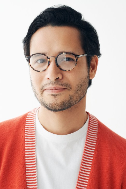 Man wearing tortoiseshell glasses, white t-shirt, and red striped cardigan by Bottega Veneta.