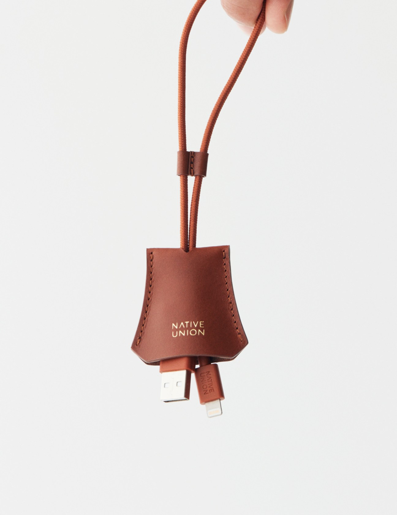 Native Union tag cable in terracotta leather with orange cord hanging from hand.
