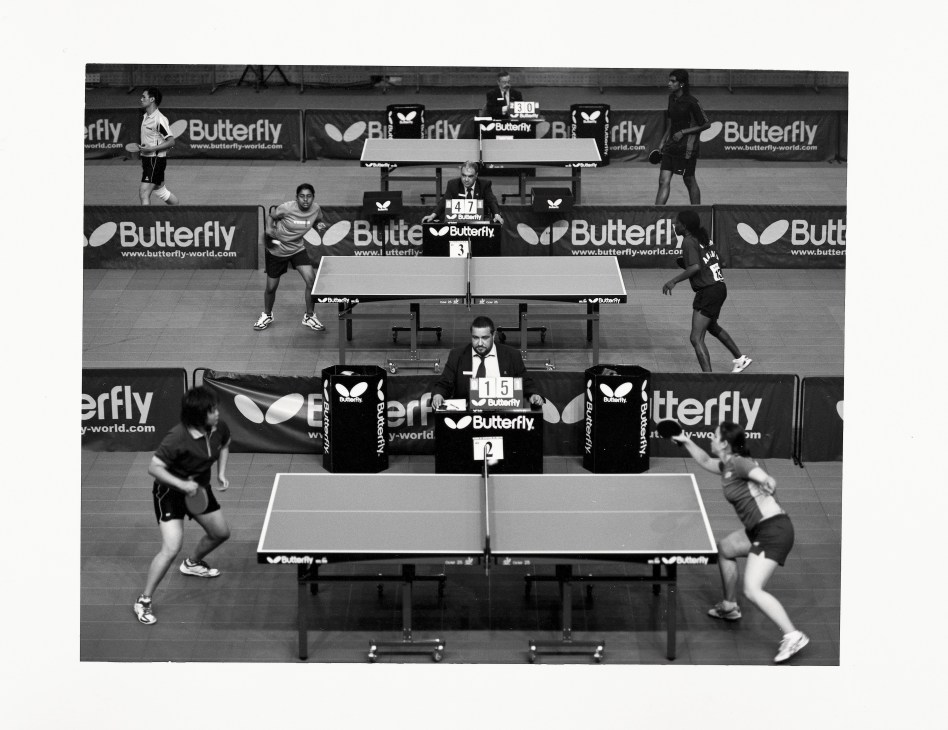 Table tennis players compete in early-stage rounds at the Jogos da Lusofonia games with Butterfly-branded tables and sponsorship signage visible.