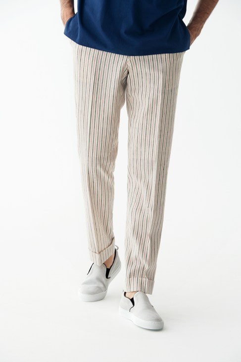 Man wearing striped beige trousers by Orazio Luciano and white slip-on trainers by AMB.