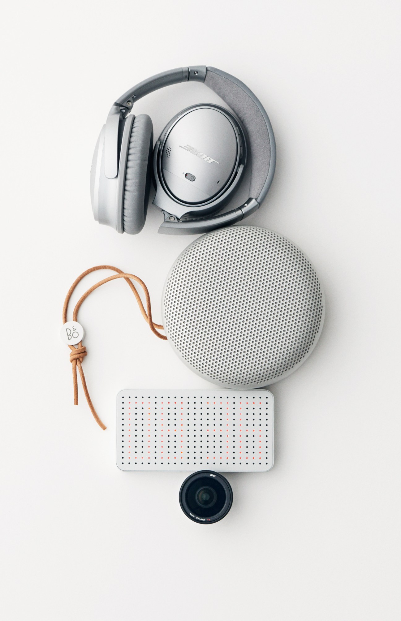 Bose headphones, Bang & Olufsen speaker, Power Cube Pro battery, and ExoLens Pro lens arranged on white background.