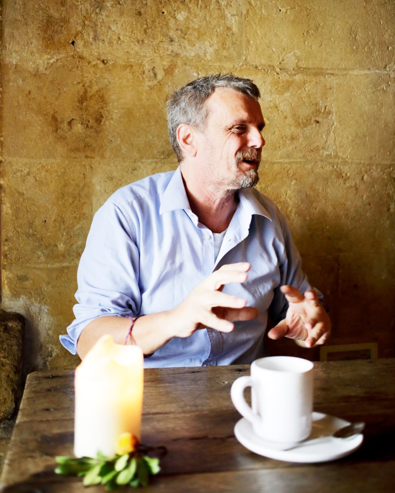 Daniele Kihlgren, founder of Sextantio hotel, gestures while speaking at a wooden table against a stone wall.