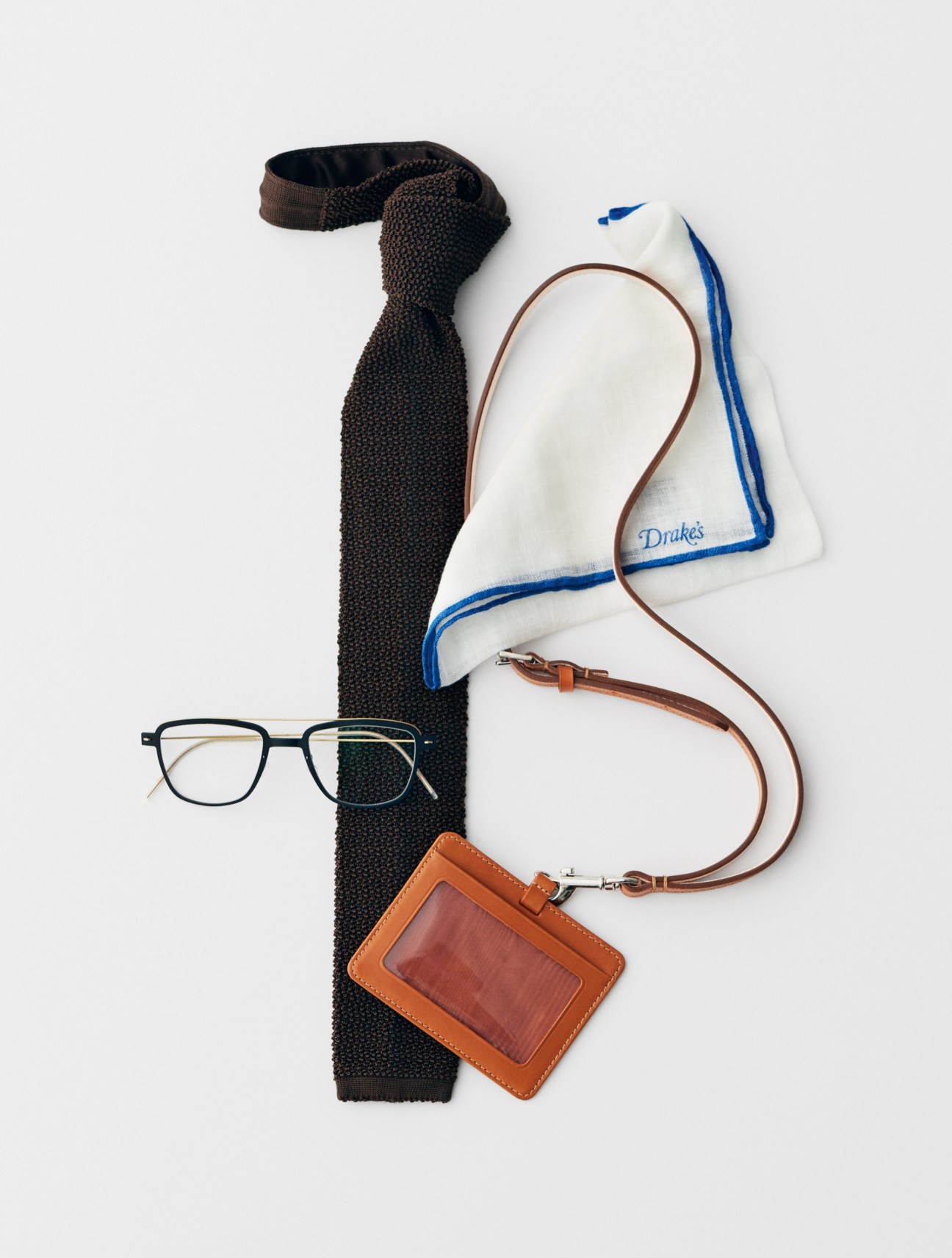 Drake's tie, Whitehouse Cox ID holder, and Lindberg glasses arranged on white background.
