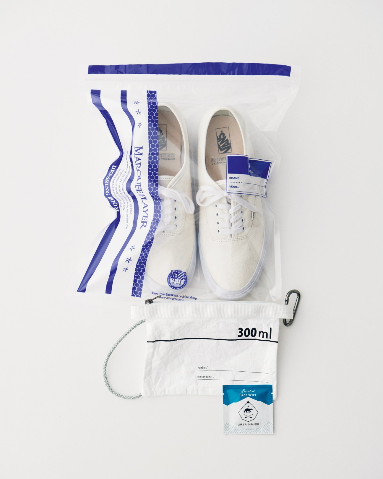 Overhead shot of white Vans trainers with blue striped packaging, travel pouch, and Ursa Major face wipes on white background.