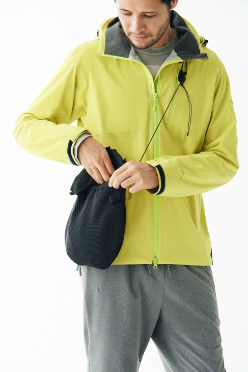Man in bright yellow Helly Hansen jacket holding black Alk Phenix bag.