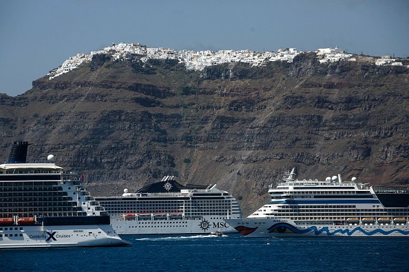 Large cruise ships sailing in blue waters past Santorini's white-washed cliffside buildings.