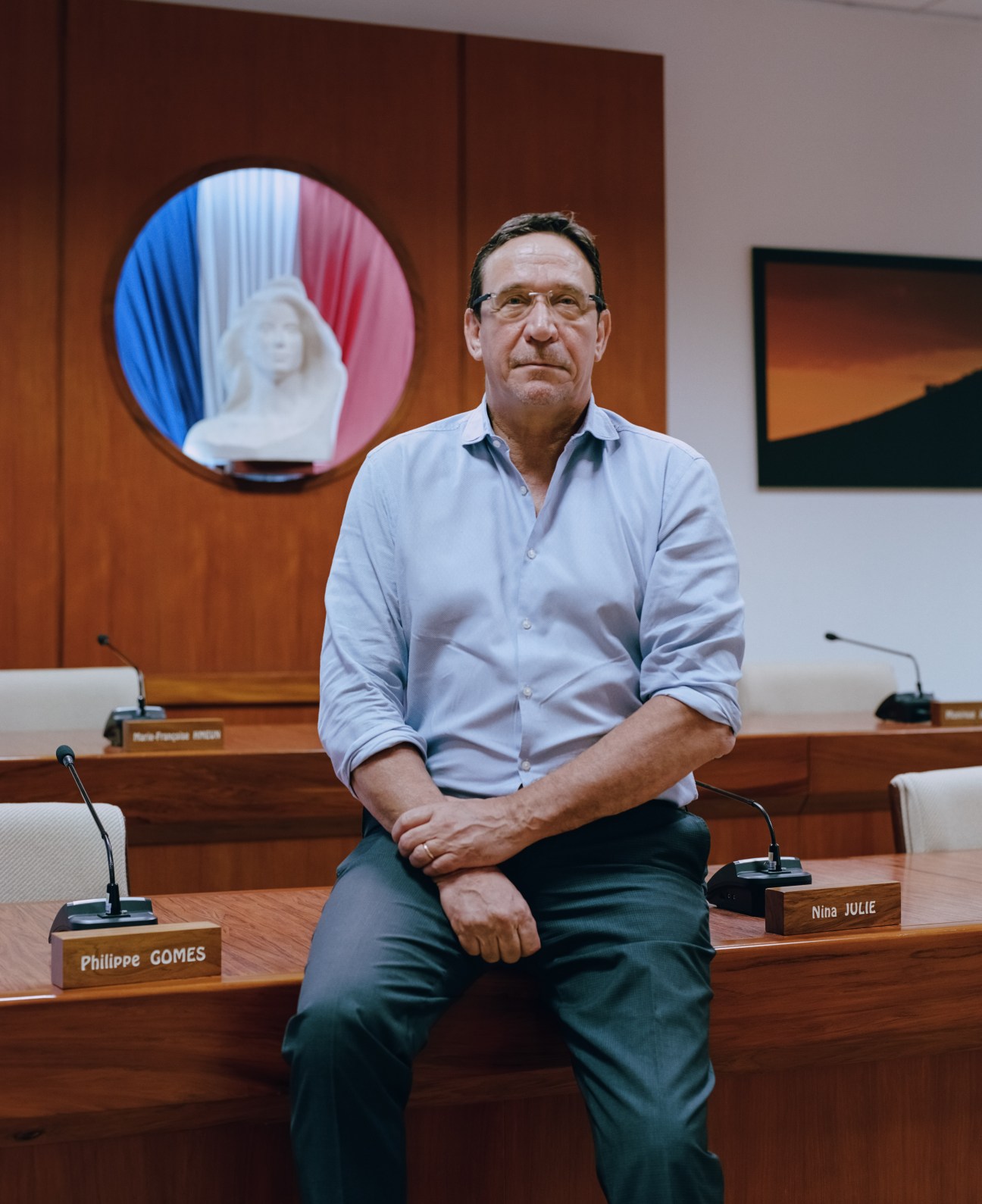Philippe Gomès, leader of Calédonie Ensemble, sits in a government chamber with a French flag bust behind him.
