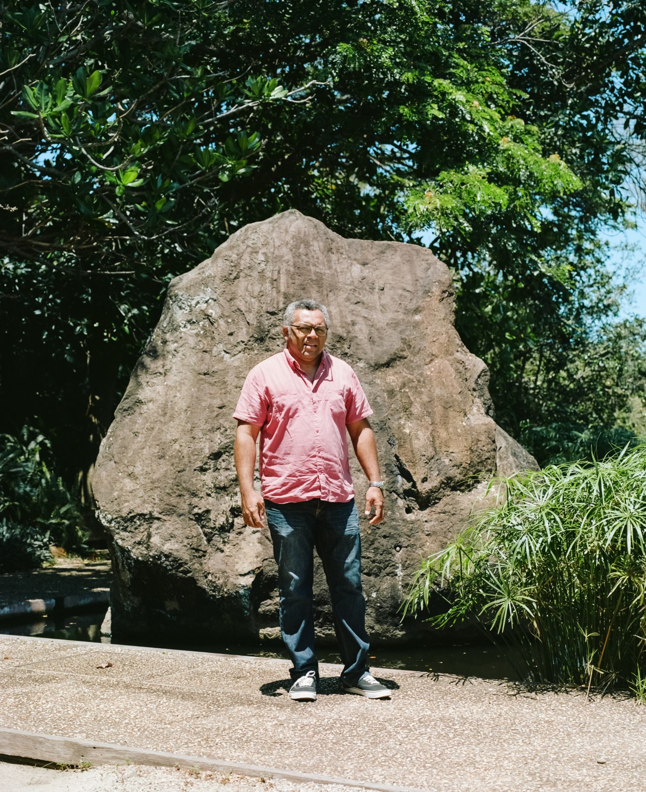 Man in pink shirt standing before large stone monument surrounded by tropical vegetation