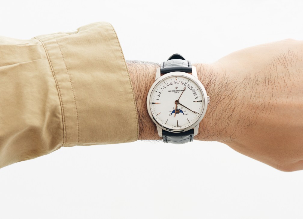 Wrist wearing a Vacheron Constantin watch with white dial and leather strap, paired with a beige shirt cuff.
