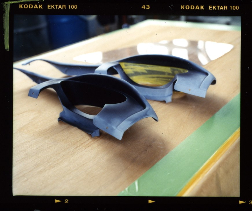 Blue car body panels and parts displayed on a wooden work surface at Mitsuoka's factory.