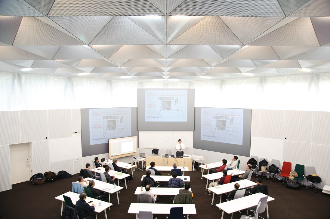 Training room with triangular ceiling, projector screens, and colored chairs arranged for seminar participants.