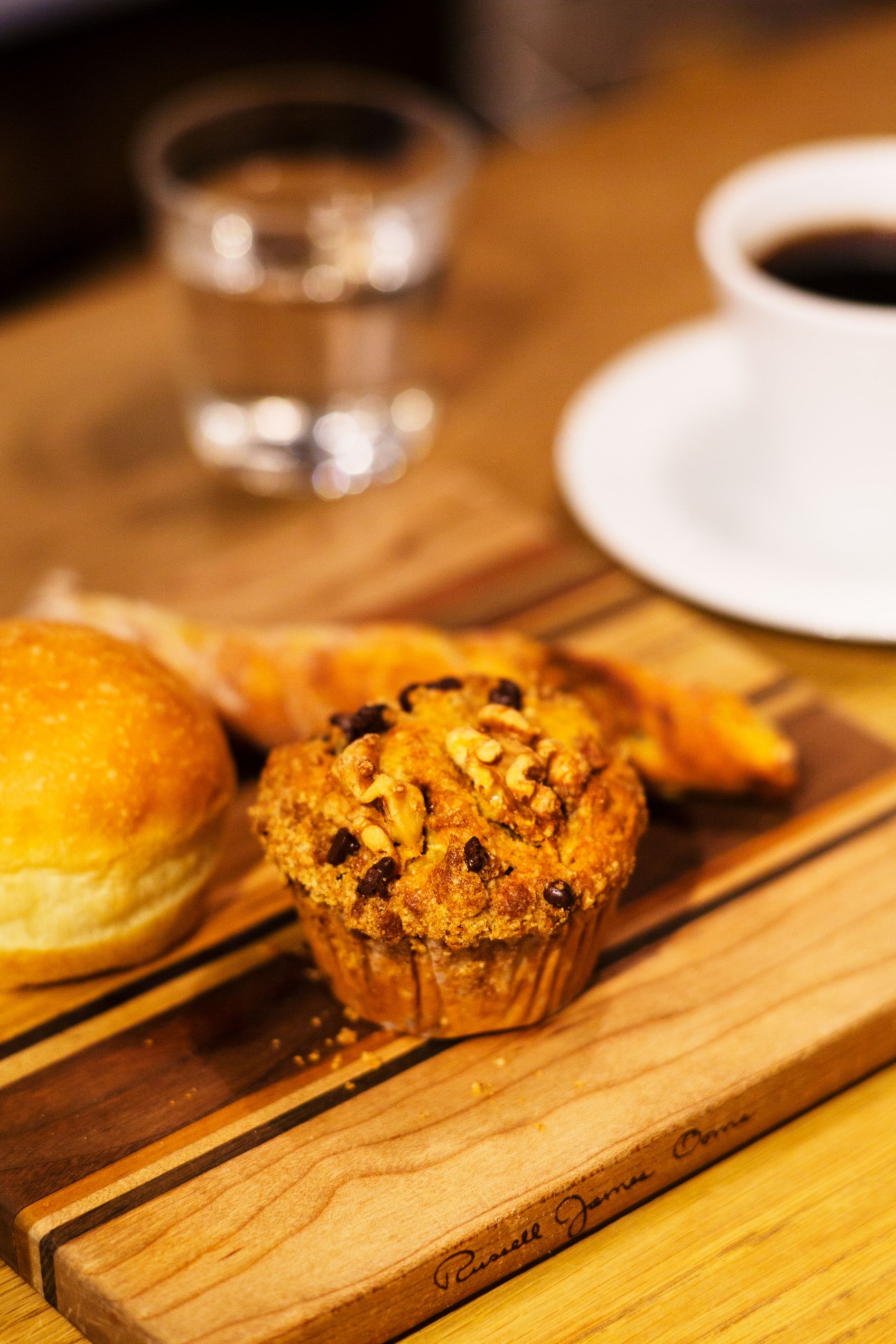 Chocolate chip muffin on a wooden board with coffee cup and plate in background