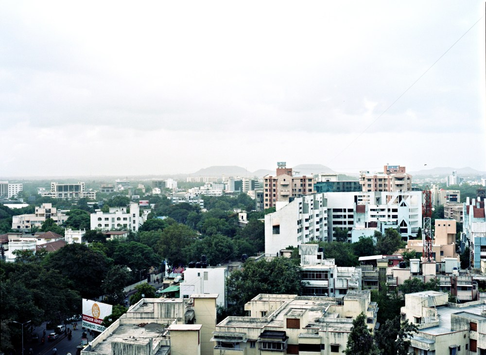 Aerial view of Pune showing mixed residential and commercial buildings with green trees and hills in the distance.