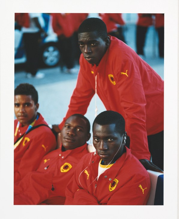 Angolan football players in red Puma tracksuits watch the opening ceremony celebrations.