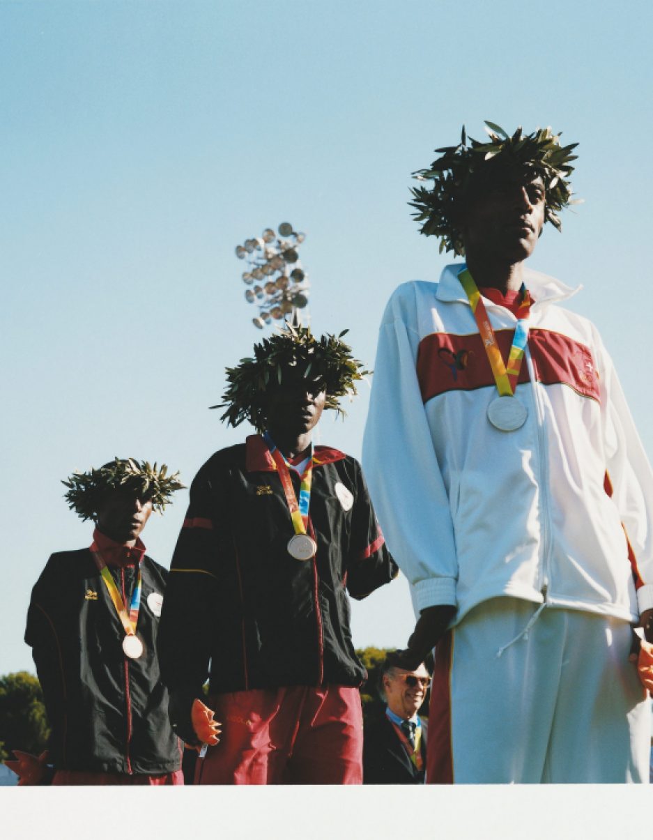 Three athletes stand on a podium at the Paralympics Games holding national flags and commemorative items.