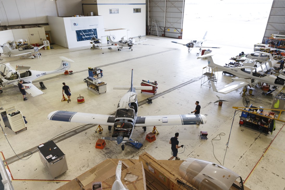 Overhead view of a busy aircraft hangar at Flight Training Adelaide with multiple small planes undergoing maintenance and training activities.