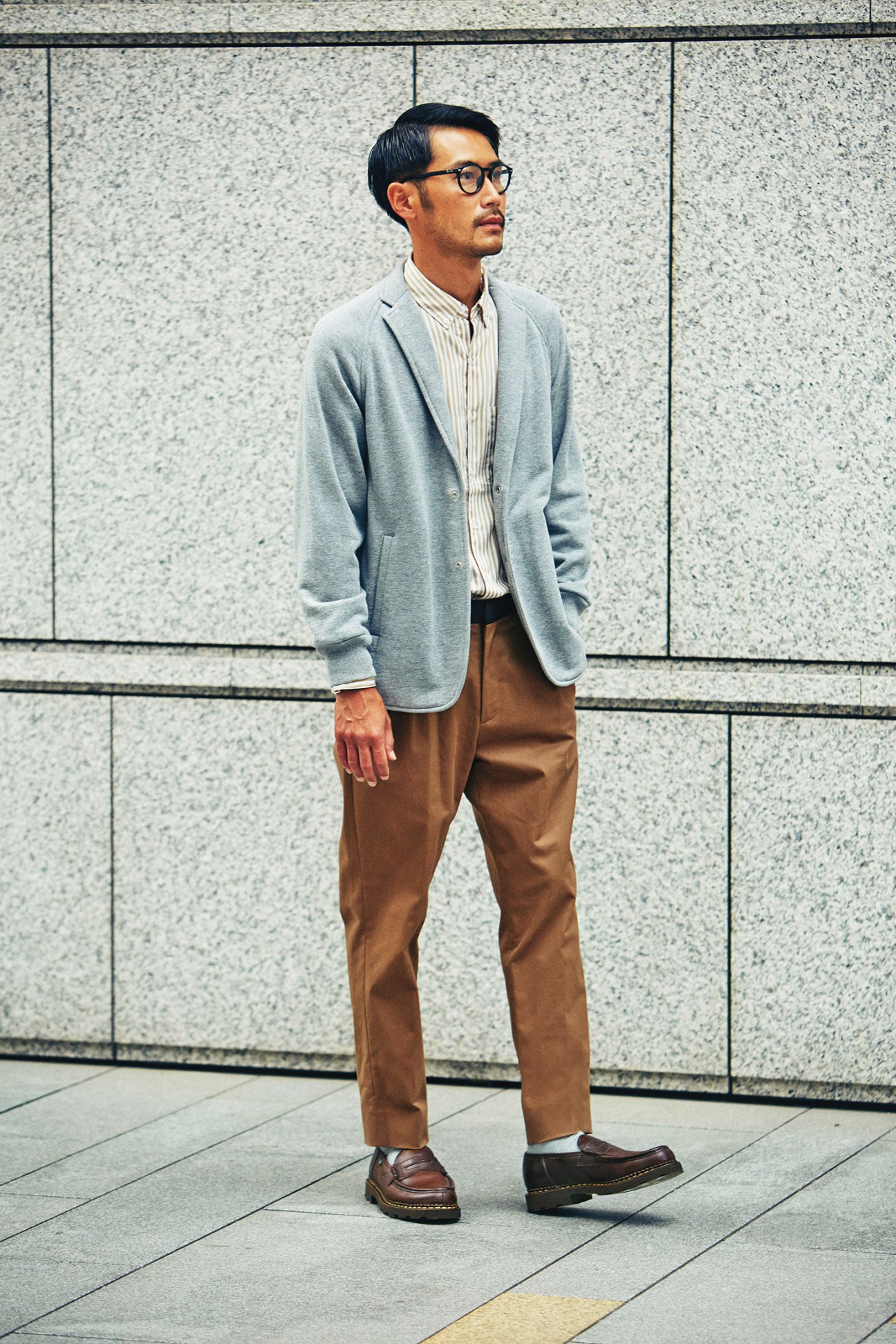 Man wearing grey Scye jacket, striped Steven Alan shirt, and brown GBS trousers with Paraboot shoes against textured wall.