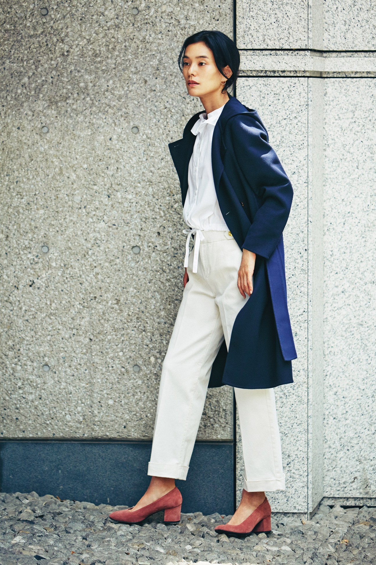 Woman wearing navy Sealup coat, white Atlantique Ascoli shirt, and cream Scotch & Soda trousers with terracotta Aeyde shoes.